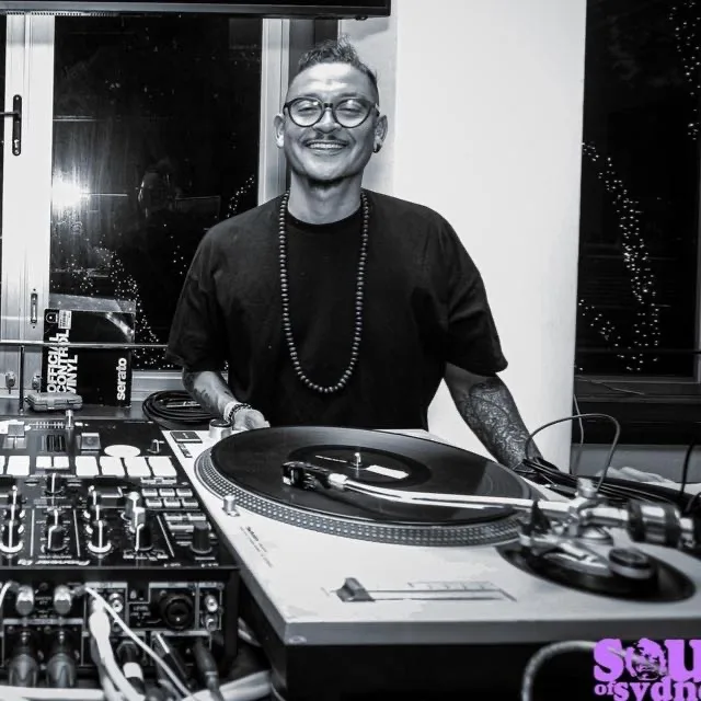 DJ CMAN smiling behind the turntables, black and white