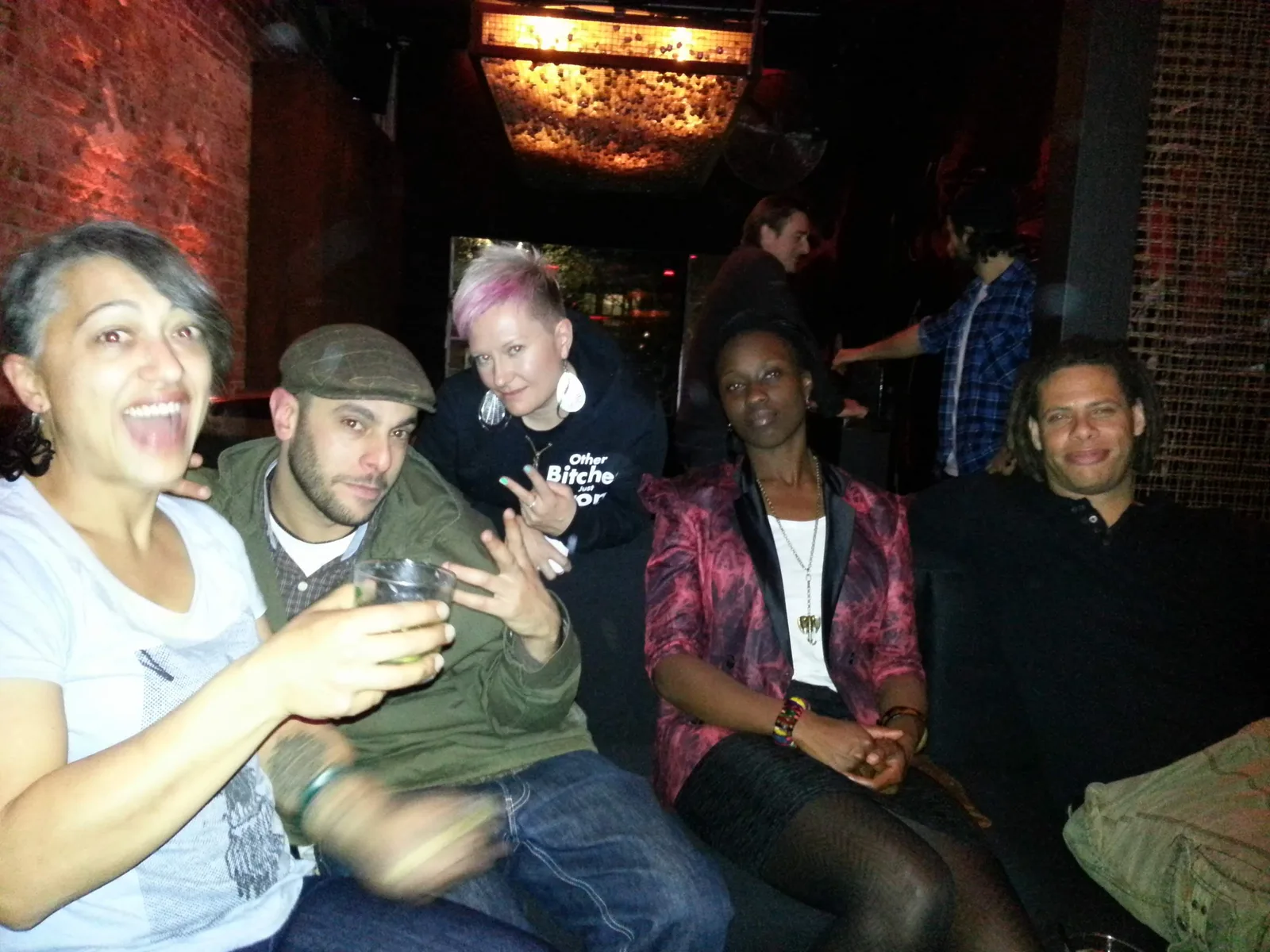 Five people crowded together on a couch at Ching-a-Lings, drinks in hand, laughing at the camera