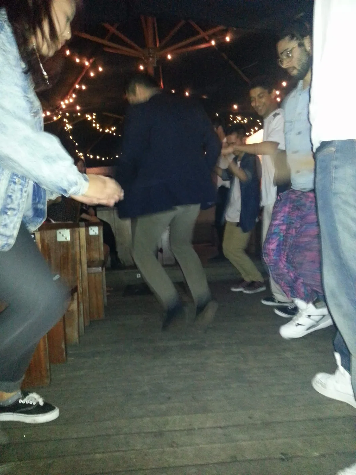 People dancing on a bench under festoon lights in the Ching-a-Lings courtyard