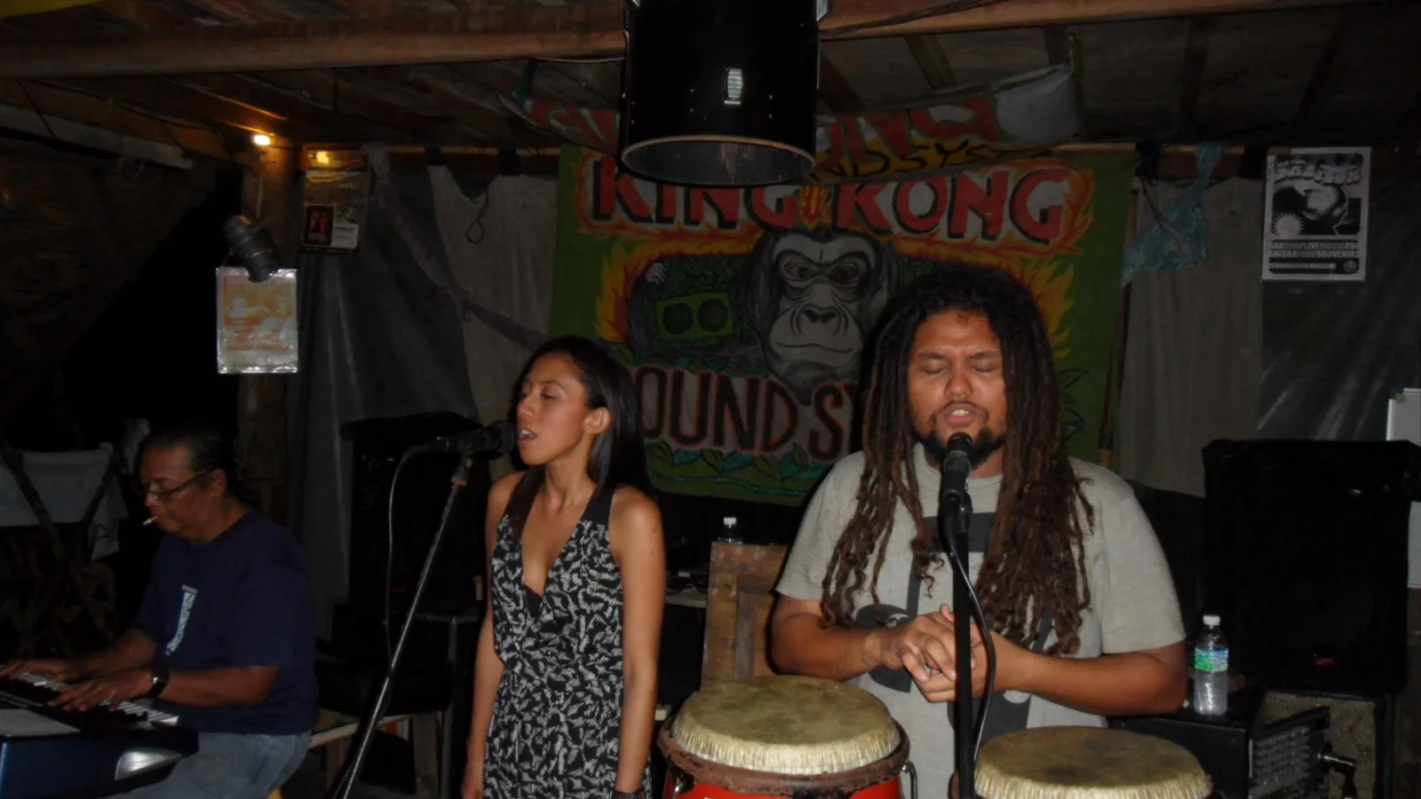 Live musicians playing congas and singing in front of a hand-painted King Kong Sounds banner