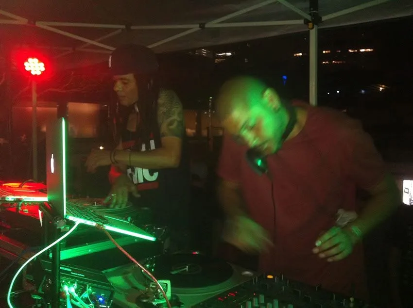 DJ CMAN and JuzzLikeDat trading records back to back under a marquee at night.