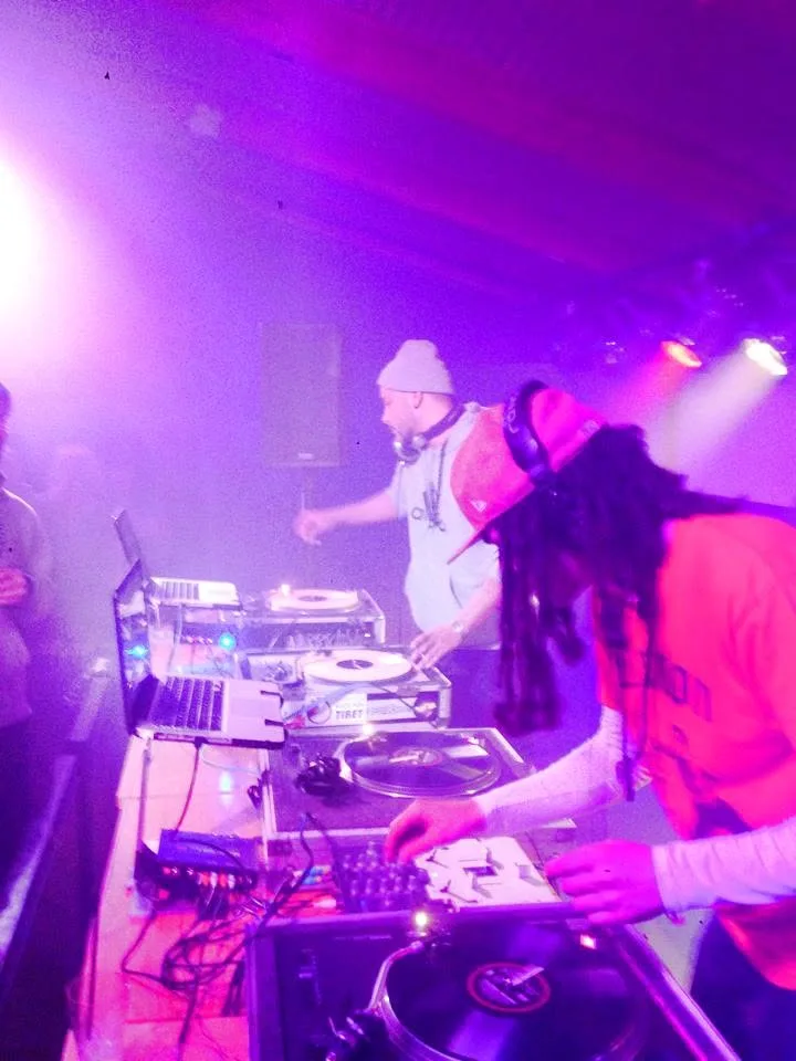 Four turntables between them, DJ CMAN reaching across as JuzzLikeDat rides the crossfader.