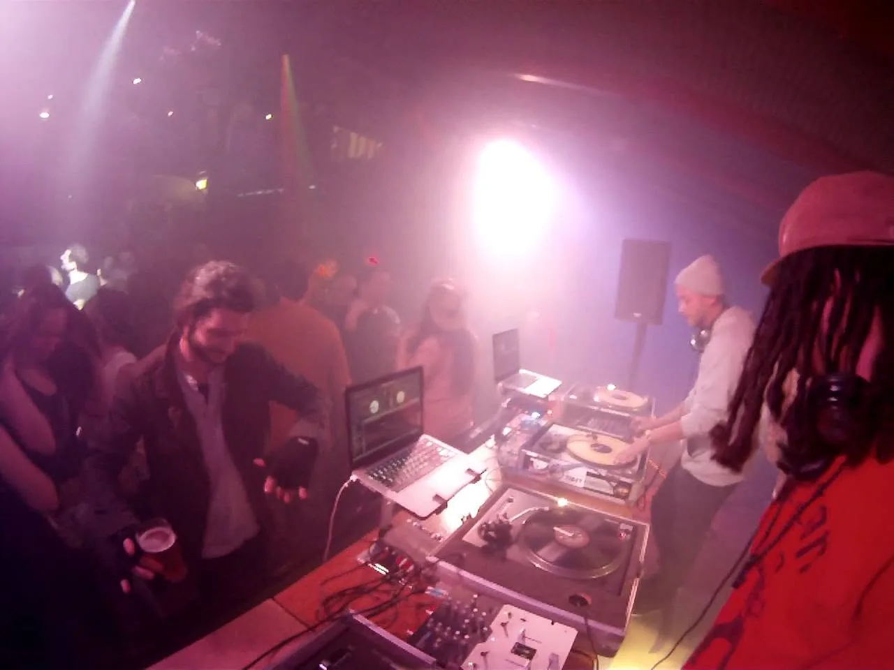 DJ CMAN and JuzzLikeDat working four turntables while a packed dancefloor crowds the booth.