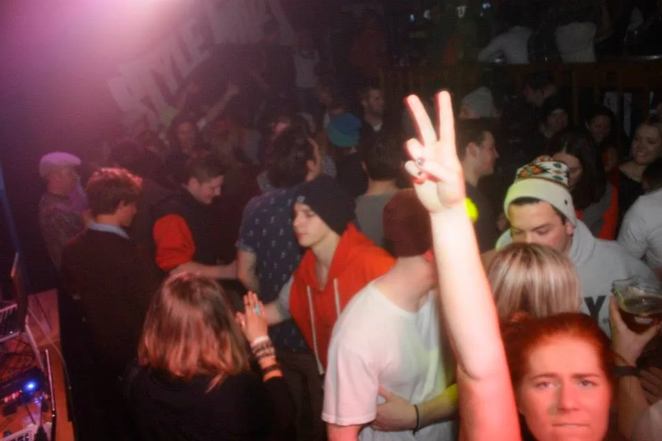 The crowd with hands raised in front of the DJ booth
