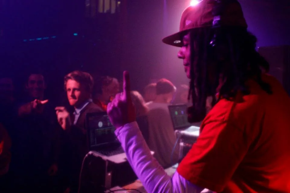 A crowded dancefloor under purple light in front of the DJ booth