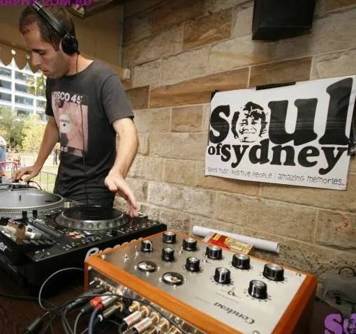Phil Toke at the turntables and a rotary mixer in front of a Soul of Sydney banner