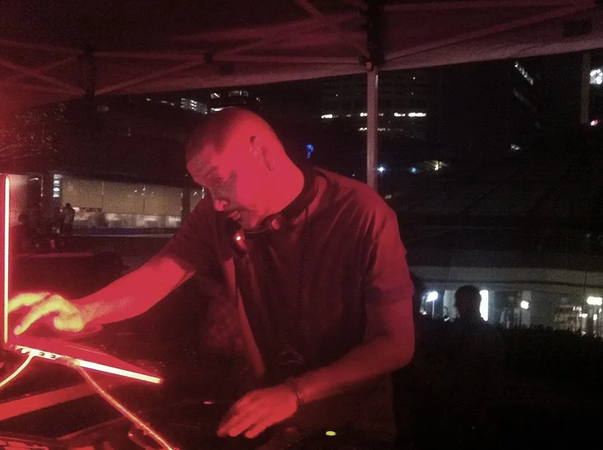 A DJ leaning into the mixer under deep red light