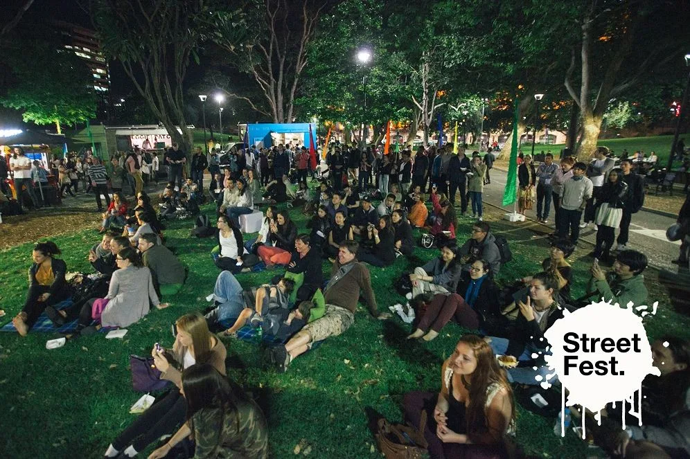 A daytime crowd sitting out on the grass at Street Fest