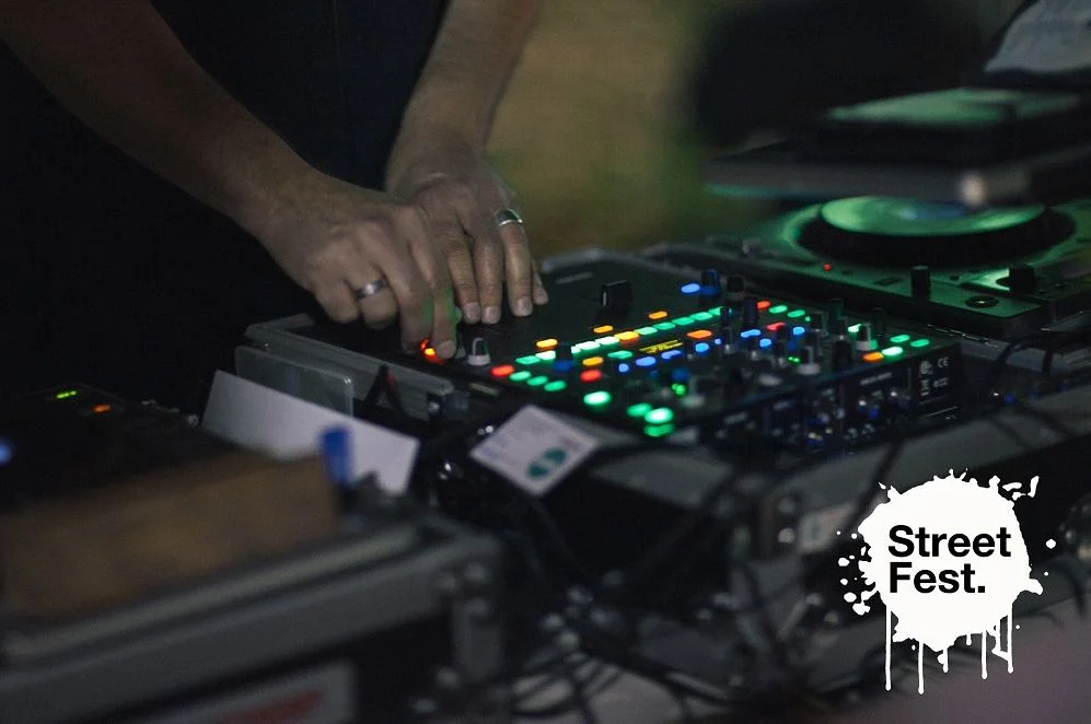 Close-up of a DJ's hands working a mixer lit with coloured buttons at Street Fest