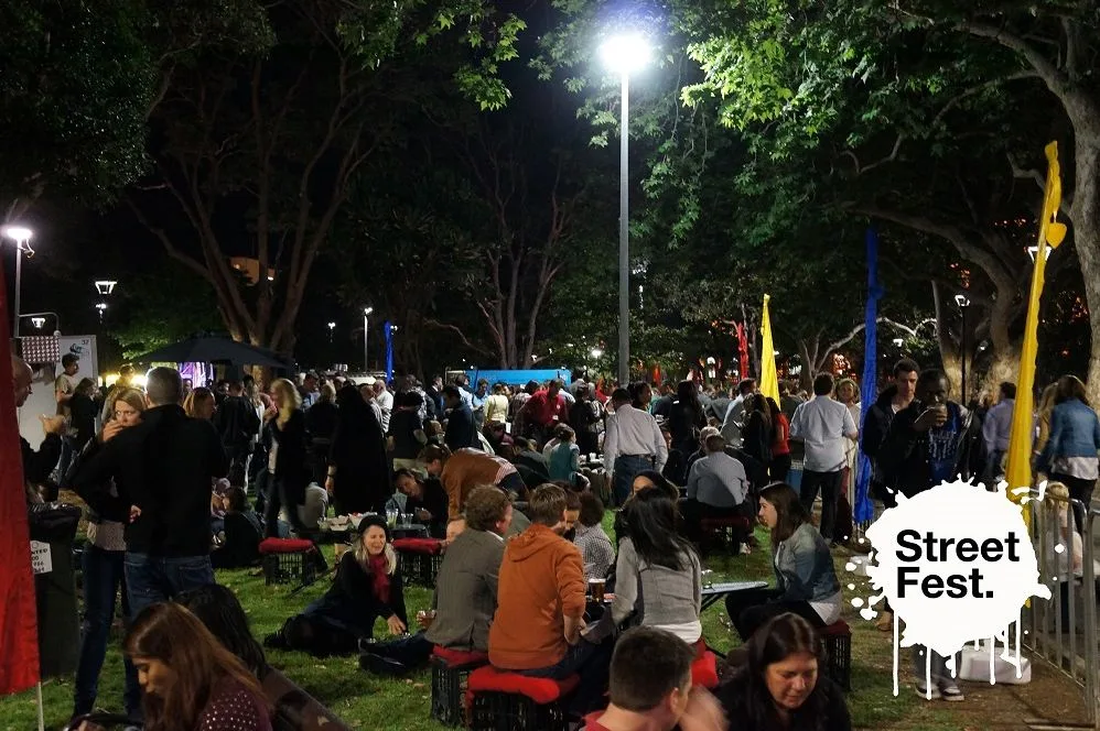 Punters gathered on the grass in the evening with the city behind