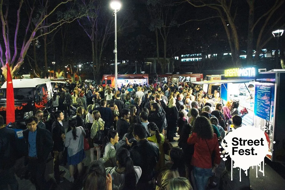A night crowd spread across the park between lit food trucks