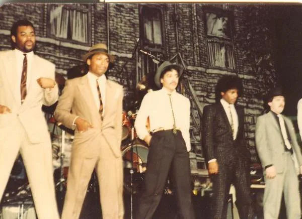 A group portrait of four musicians in pale suits