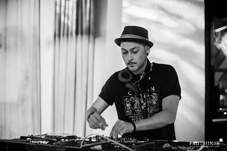A black and white shot of DJ CMAN in a hat behind the decks