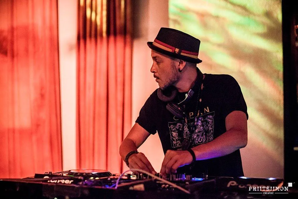 A DJ in a hat playing in front of a red curtain at the festival