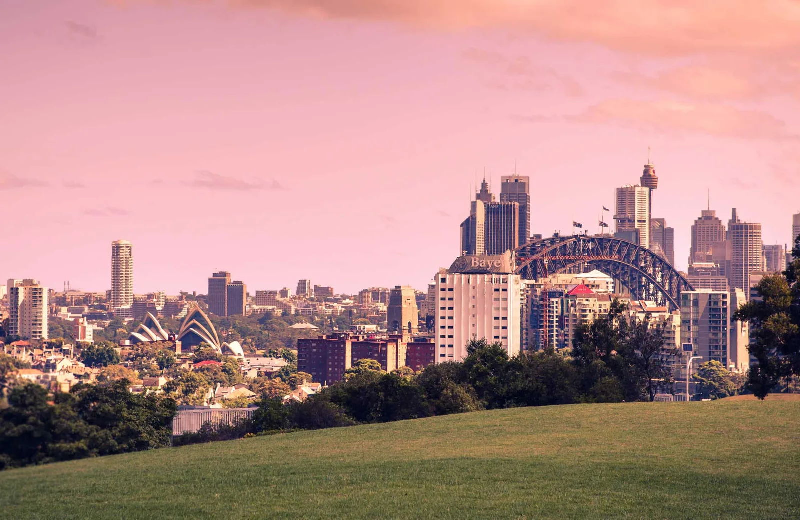 Sydney skyline at dusk with the Harbour Bridge and Opera House seen across parkland