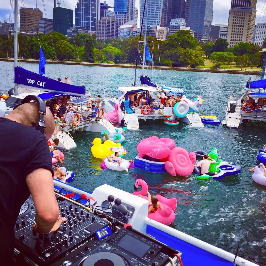 A DJ playing on deck surrounded by boats and inflatables on the harbour
