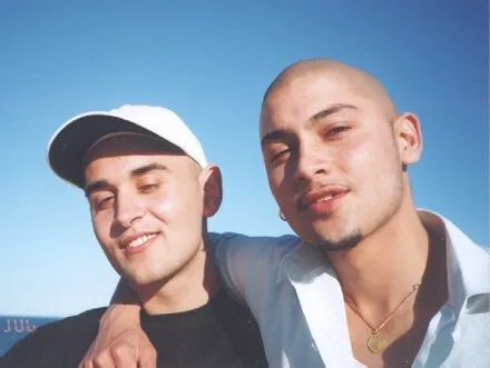 DJ CMAN and DJ Daniel as young men, outdoors against a clear blue sky