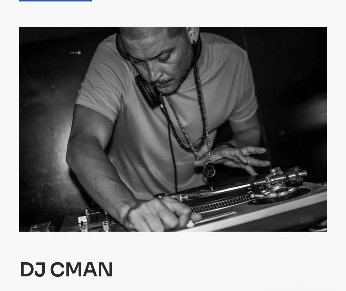 A black and white portrait of DJ CMAN behind the decks