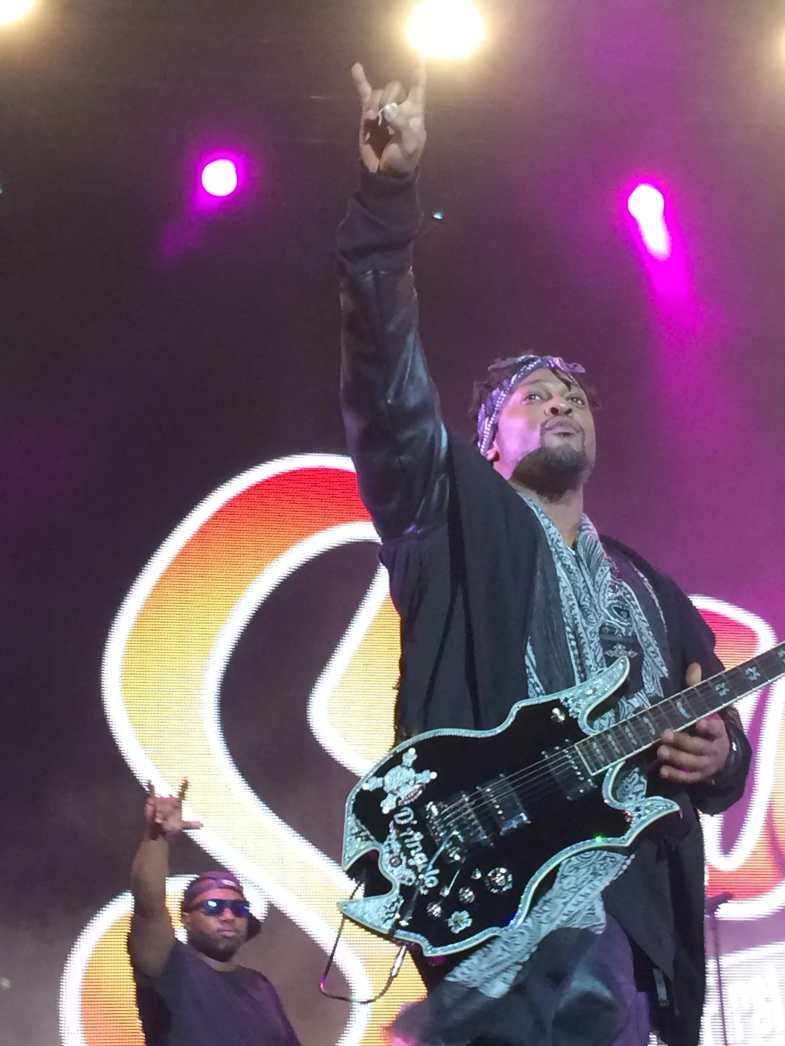 D’Angelo in a headscarf raising his fist to the sky, crystal-edged guitar slung on, Soulfest screen glowing behind