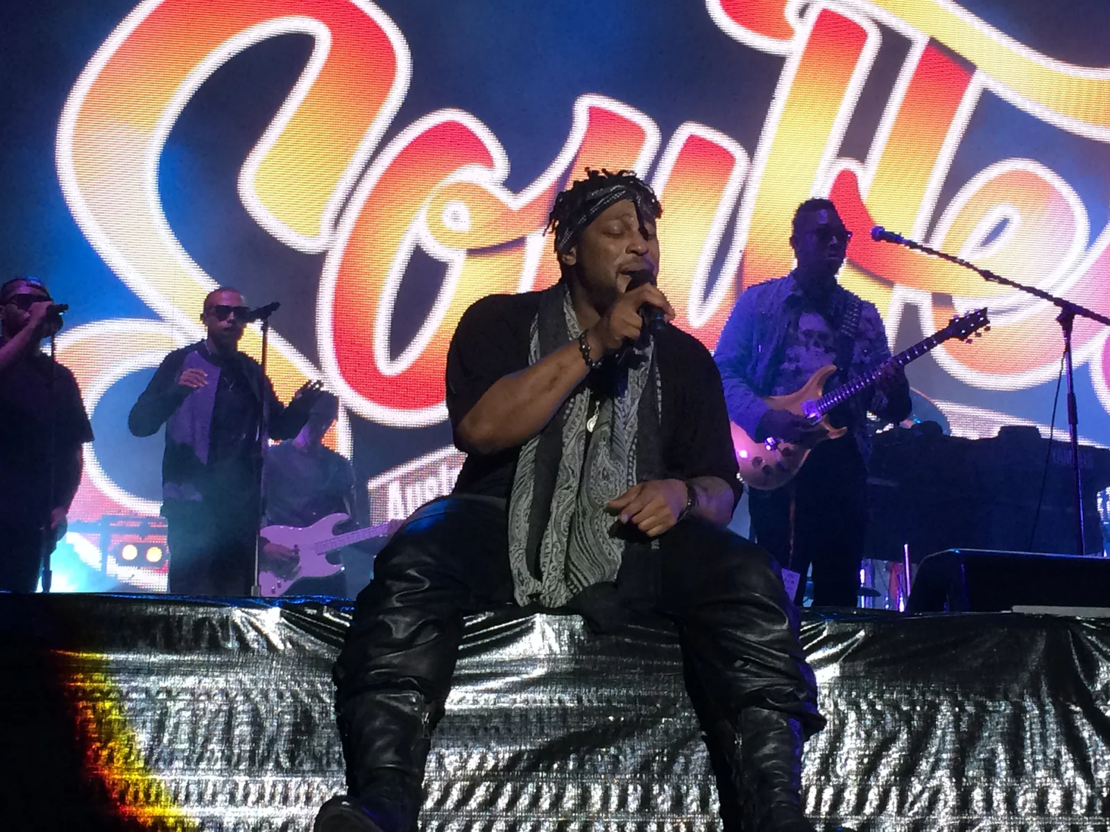 D’Angelo seated at the edge of the stage singing into the mic, his band and the Soulfest lettering behind