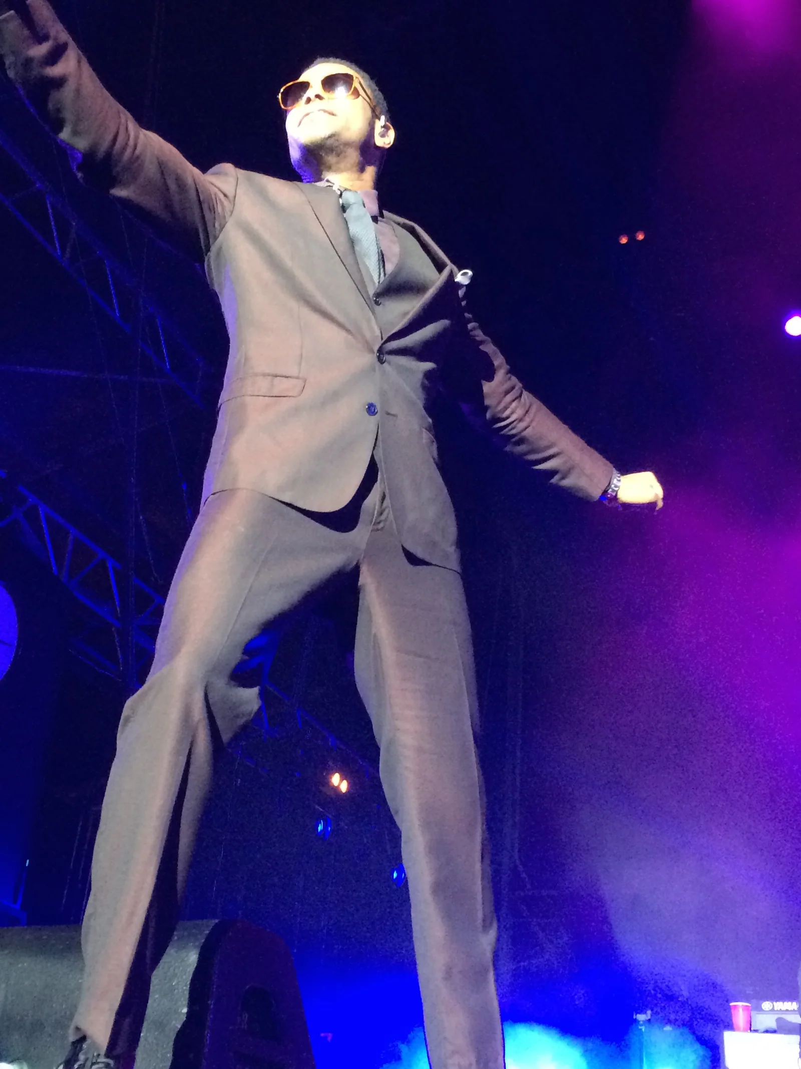Maxwell in a suit and orange sunglasses reaching out over the crowd, shot from below the stage