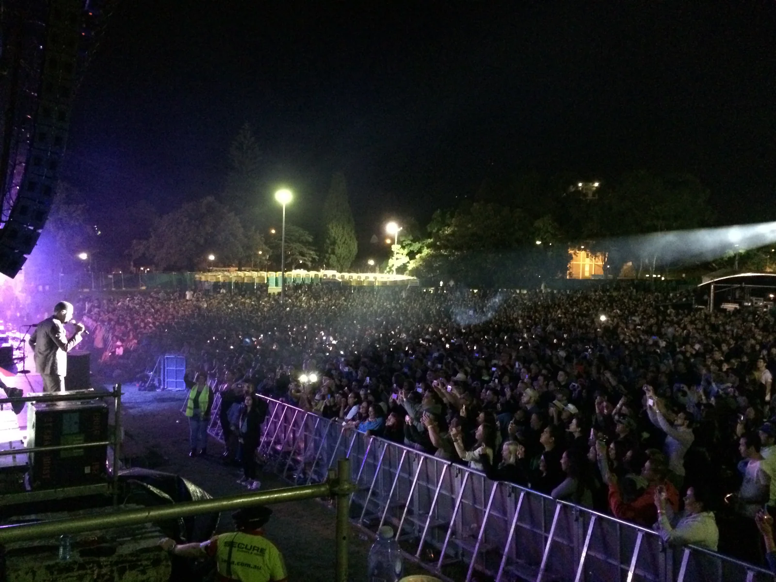 The Victoria Park night crowd shot from the DJ booth, Maxwell at the mic under the stage lights, phones out along the barrier